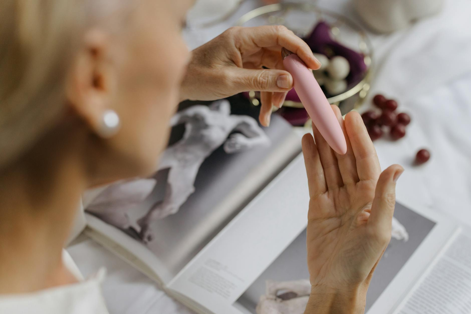 A person holding a pink vibrator with art books nearby, symbolizing intimate self-exploration and personal pleasure.