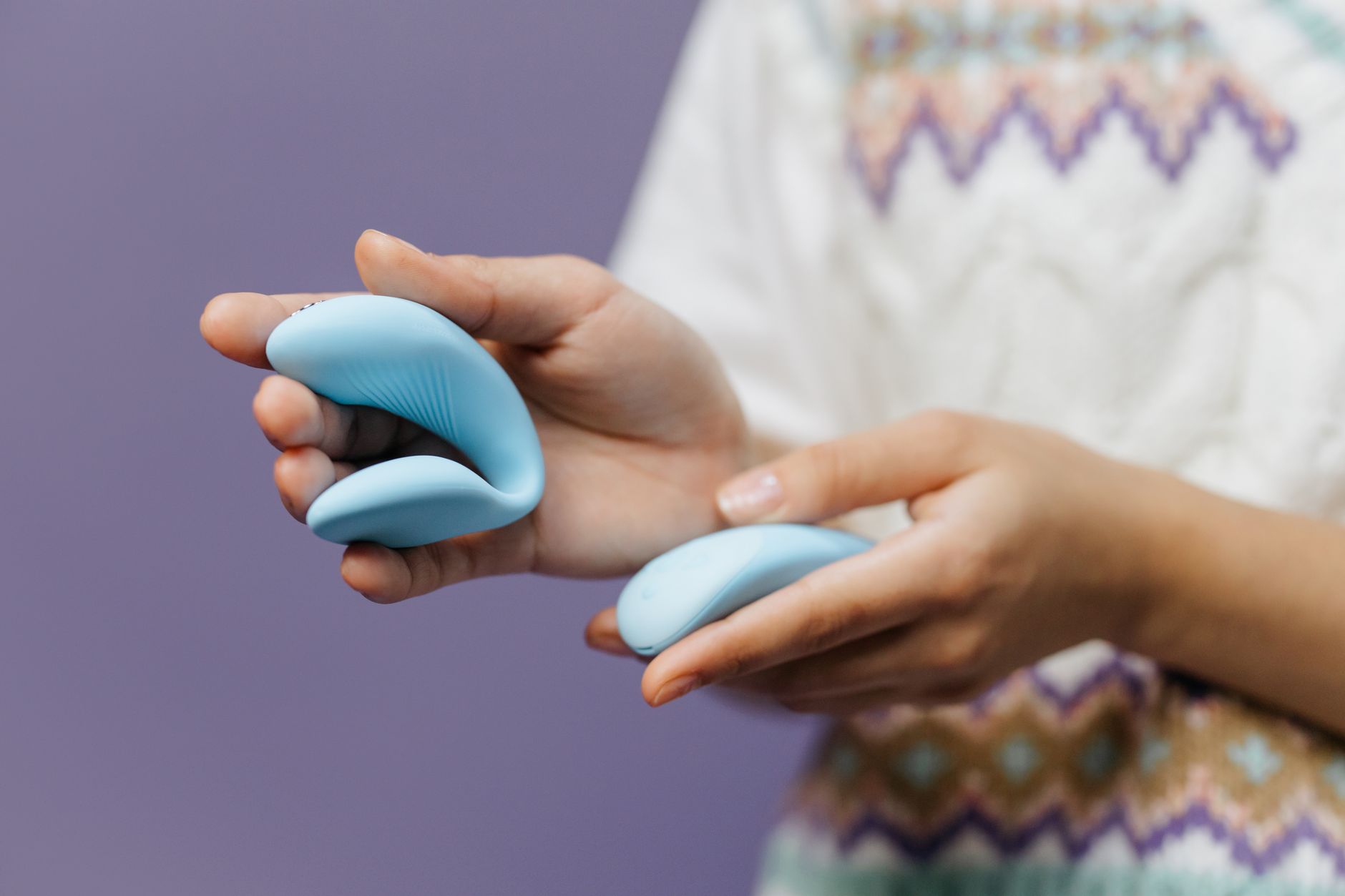 Close-up of hands holding a blue lemon vibrator against a purple background, ready to explore.