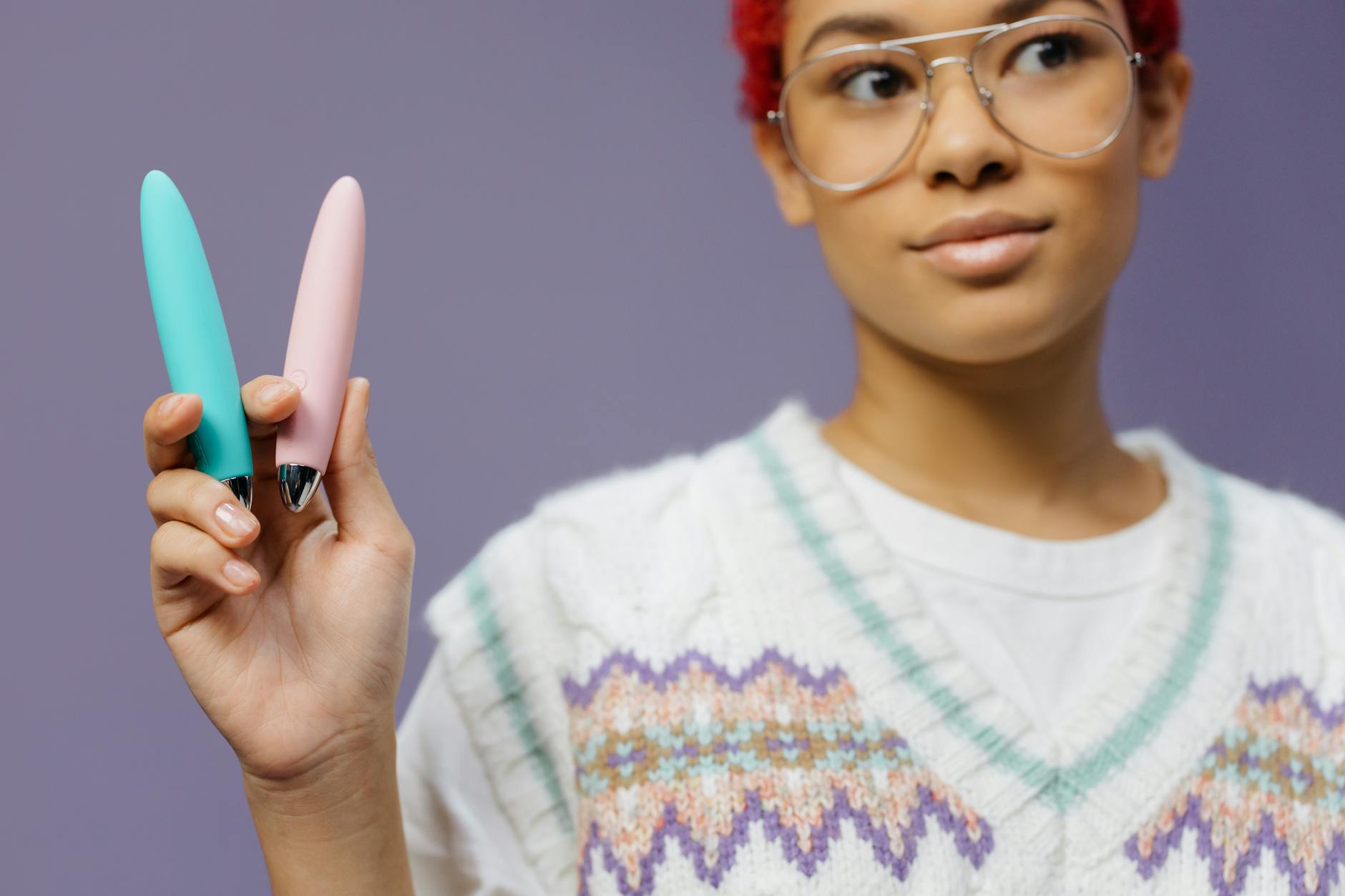 A person holding two colorful clitoral vibrators against a purple background