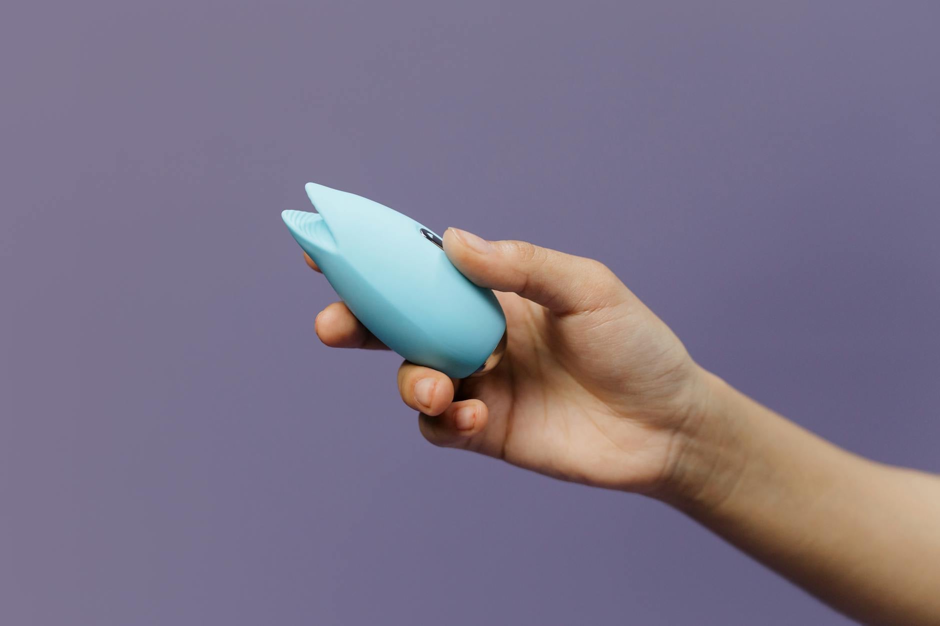 A person holding a blue clitoral vibrator in hand against a purple background, symbolizing self-empowerment and pleasure