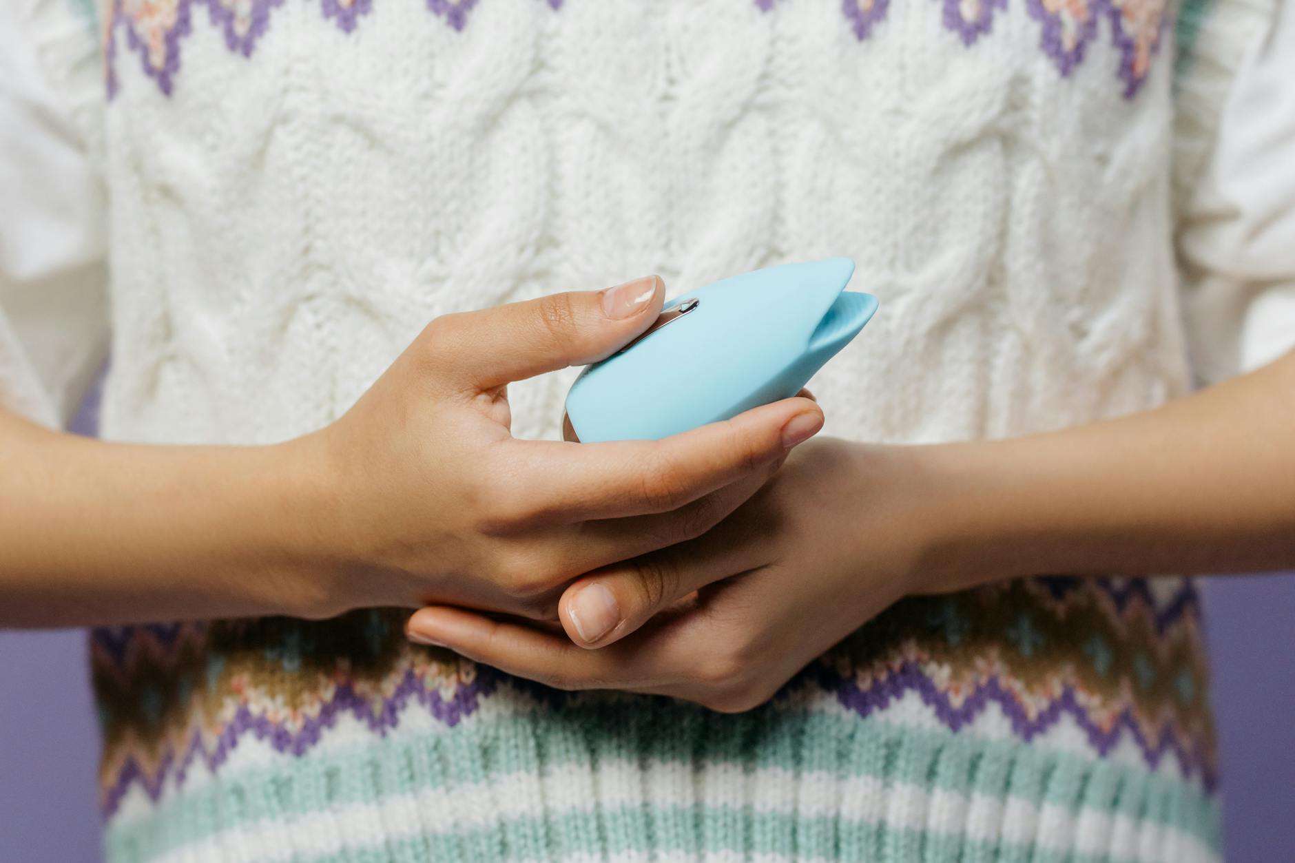 Close-up hands holding a blue personal massager against a knitted sweater