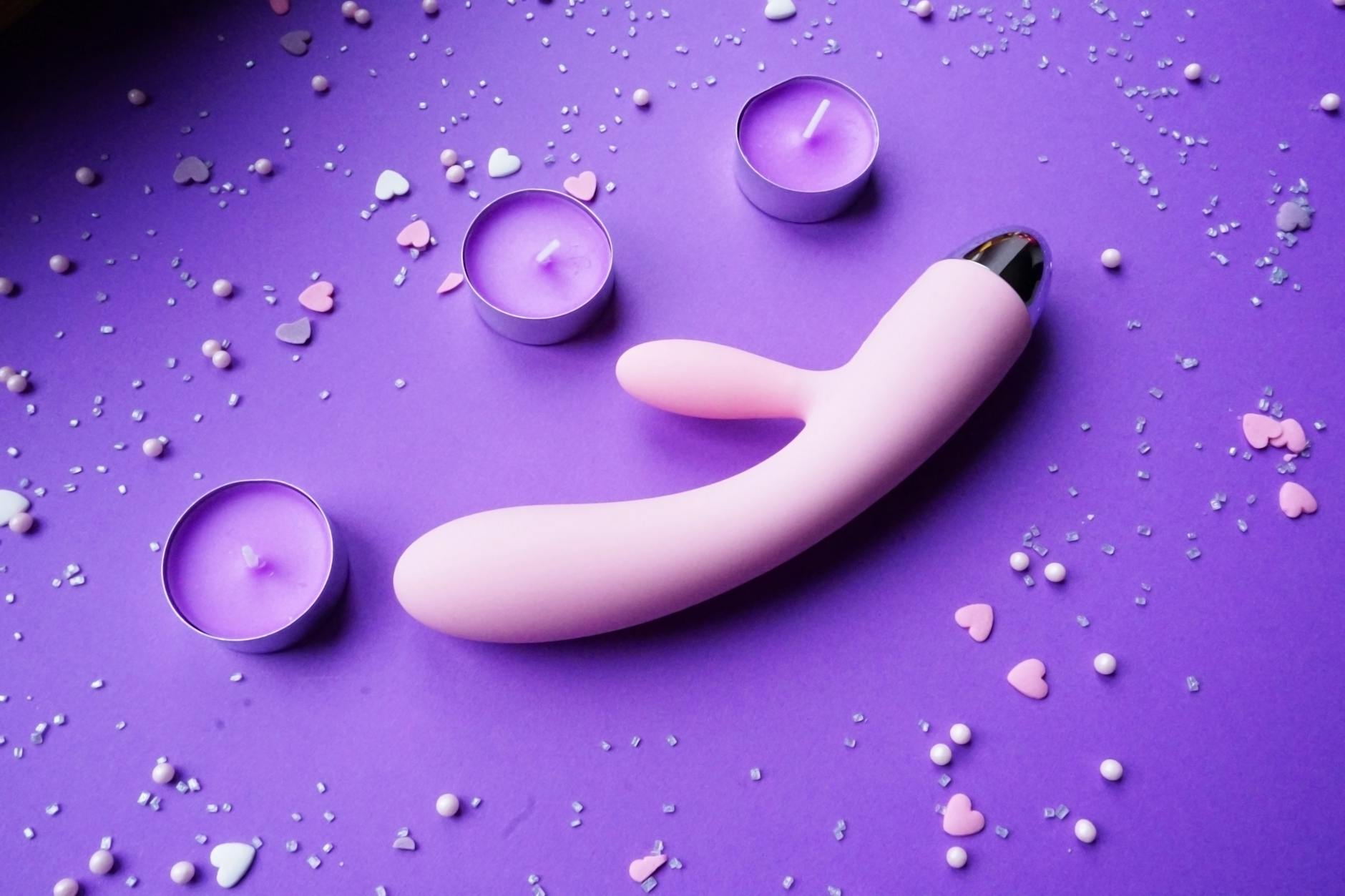 Pink lemon vibrator on purple background with heart confetti and candles for romantic setting